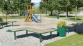 Banc sans dossier public Nordhavn en forme de S dans un parc avec aire de jeux pour enfants.