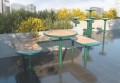 Table de bar d'extérieur Nordhavn de 70 cm avec plateau en bois et structure verte, entourée de végétation urbaine.