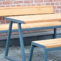 Amager 4 Seater Public Backless Bench with a sturdy metal frame and wooden seating, placed next to a brick wall.