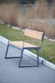 Banc Public Amager en bois et métal, trois places avec dossier et accoudoirs, sur trottoir pavé.
