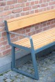 Banc Public Amager à Dossier 3 Places avec Accoudoirs en bois et métal, adossé à un mur de briques.