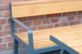 Amager 3 Seater Public Backrest Bench w/ Armrest with wooden slats and blue metal frame against a brick wall.