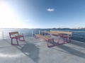 Öffentliche Sitzbank Amager 4-Sitzer mit Rückenlehne und Armlehne auf Terrasse am Wasser.