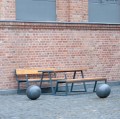Table d'extérieur Amager 150 cm avec bancs en bois et métal pour 4-6 personnes, style industriel, devant un mur de briques.