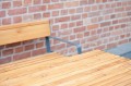 Table d'extérieur Amager 150 cm en bois avec banc, fond de mur en briques rouges.