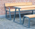 Table d'extérieur Amager 180 cm en bois avec structure en métal, adaptée pour 6 à 8 personnes, sur fond de mur en briques.
