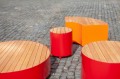 Tabouret d'extérieur Valby en métal rouge avec assise en bois sur pavé.
