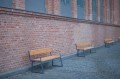 Amager 4 Seater Public Backrest Bench w/ Armrest against brick wall in urban setting.