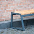 Öffentliche Parkbank Amager 3-Sitzer aus Holz und Metall an einer Backsteinmauer.