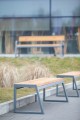 Amager 4-Sitzer öffentliche banklose Bank aus Holz und Metall im modernen Design auf einem Gehweg im Freien.