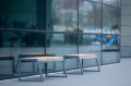 Zwei Amager 4-Sitzer öffentliche banklose Bänke aus Holz und Metall vor einem modernen Gebäude.