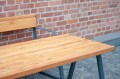 Table d'extérieur Amager en bois 180 cm, cadre en métal, fond mur de briques.