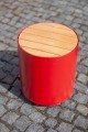 Tabouret d'extérieur Valby rouge avec assise en bois sur pavé.
