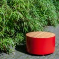 Banc Public Sans Dossier Valby | Rond en métal rouge et bois, placé sur un sol pavé près de buissons verts.