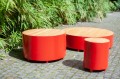 Valby Public Backless Bench | Round, red color, with wooden seating, placed on a cobblestone path near green bamboo.