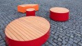 Red and orange round Valby Public Backless Bench set on cobblestone pavement.