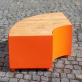 Viertelrunde Valby Öffentliche rückenlose Bank aus Holz und Metall auf Pflastersteinen.