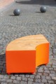 Banc Public Sans Dossier Valby Quart de Rond en bois et métal orange sur un sol pavé.