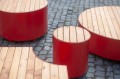 Valby Öffentliche Rückenlose Bank | Viertelrund aus rotem Metall und Holz auf Kopfsteinpflaster.