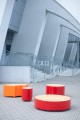 Valby Öffentliche Rückenlose Bank in Rot und Orange vor einem modernen Gebäude.