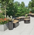 Banc Public Sans Dossier Valby Carré dans un jardin moderne entouré de plantes et d'arbres.