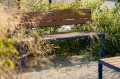 Frederiksberg 3 Seater Public Backrest Bench in a garden setting surrounded by plants.