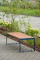 Banc public sans dossier à 3 places Frederiksberg en bois et métal sur un trottoir pavé.