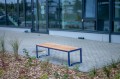 Banc public sans dossier à 3 places Frederiksberg en bois et métal sur une terrasse pavée.