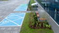 Banc public sans dossier à 3 places Frederiksberg près d'un jardin paysager, à côté d'une zone de parking accessible.