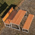 Frederiksberg 4-Sitzer öffentlicher rückennloser Bank aus Holz und Metall auf Gehwegplatten im Freien.