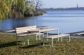 Banc public sans dossier 4 places Frederiksberg en bois et métal sur l'herbe près d'un lac.