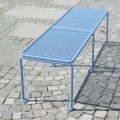 Banc public sans dossier Østerbro 3 places en métal bleu sur trottoir pavé.