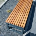 Hellerup 4 Seater Public Backless Bench with wooden slats and metal frame placed on gravel.