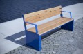 Holzbank Indre By 4-Sitzer mit blauen Metallrahmen, Rückenlehne und Armlehnen an der Uferpromenade.