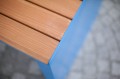 Close-up of Indre By 4 Seater Public Backless Bench, showcasing wooden slats and blue metal frame.