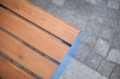 Tabouret d'extérieur Indre By en bois avec structure métallique bleue sur sol pavé.