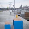 Table d'extérieur Indre By 180 cm avec bancs bleus en bois sur une promenade moderne.