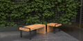 Tabouret d'extérieur Vesterbro en chêne avec pieds en métal, placé sur une terrasse avec mur de verdure en arrière-plan.