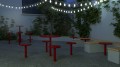 Table de bar d'extérieur Sydhavn rouge dans un jardin avec guirlandes lumineuses.