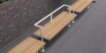 Holmen 3 Seater Public Backless Bench made of wood with metal legs and a central handrail installed on an urban pavement.
