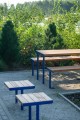 Tabouret d'extérieur Holmen en bois avec pieds en métal bleu sur fond de jardin.