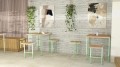 Holmen Outdoor Bar Stool in a modern cafe setting with matching tables and hanging plants.