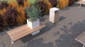 Une poubelle de rue Holmen en bois et métal à côté d'un banc public et d'un parterre de buissons colorés.