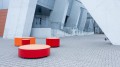 Valby Public Backless Bench | Quarter Round in red and orange placed outside a modern building.
