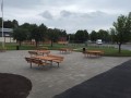 Banc et table en acier galvanisé sur une place publique, entourés d'arbres et de bâtiments.