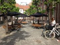 Outdoor seating area with Square Bench &amp; Table under black umbrellas in a courtyard.