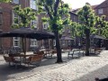 Tables et bancs en bois sous parasols noirs sur une place pavée.