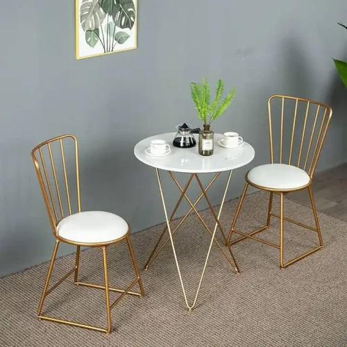 Deux chaises en métal doré avec assises blanches autour d'une table ronde moderne, décor bureau.