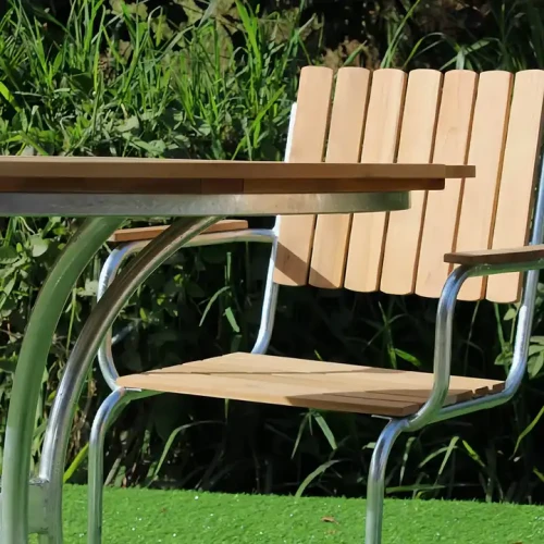 Modern metal frame wood seating stackable dining chair next to a table in a garden.