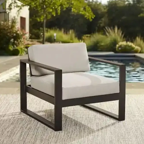 Modern black metal chair with beige cushions by a poolside.